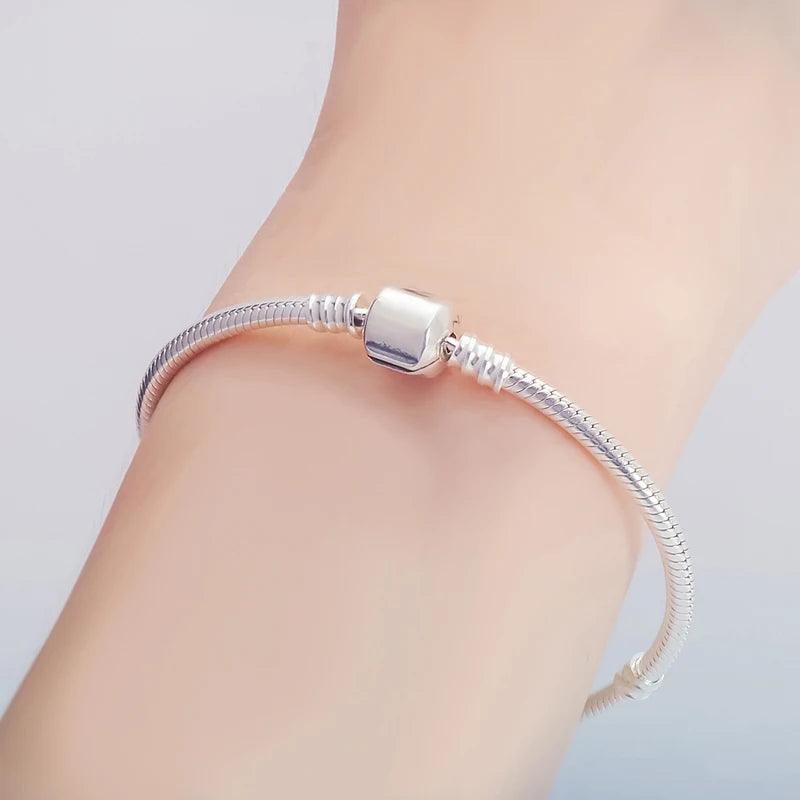 A close-up of the Tibetan Silver Charm Bracelet, known for its never-fading design and timeless elegance, on a wrist. The bracelet showcases a sleek look with a cylindrical clasp and smooth, flexible links that create a minimalist and sophisticated appeal. The background features a soft gradient of light colors.