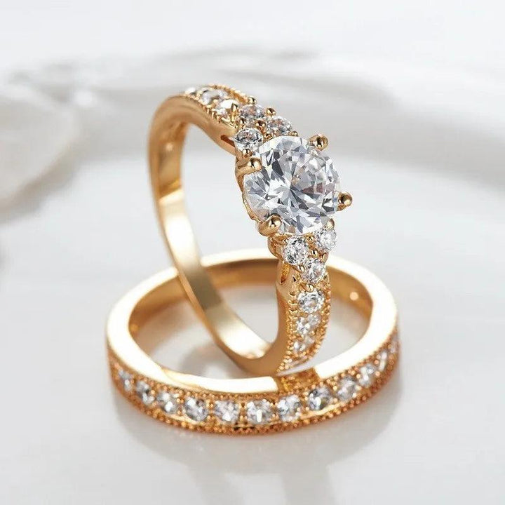 Two yellow gold color rings are decorated with dazzling cubic zirconia stones. One ring boasts a larger central stone accompanied by smaller ones on the band, while the other showcases a seamless row of smaller stones. These exquisite hypoallergenic jewelry pieces are gracefully displayed against a light background.