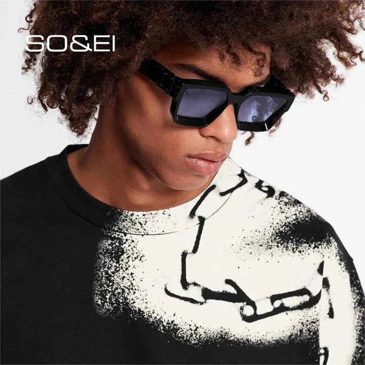 A person with curly hair is showcasing vintage luxury while wearing large black Square Men Sunglasses, which feature UV400 lenses, paired with a graphic T-shirt displaying an abstract design. The setting is a plain white background with the text "SO&EI" at the top left corner.