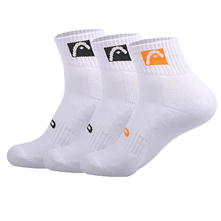 The "Sports Socks Cotton Tennis Socks Sweat-Resistant Design" come in a pack of three pairs of white athletic ankle socks, ideal for sports use. Each pair features a ribbed cuff with two socks sporting a black logo and one an orange logo. These socks are sweat-resistant, with reinforced toes and heels for added comfort and durability.