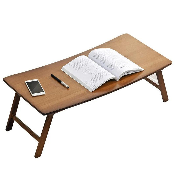 The Portable Laptop Desk Bed Tray Table Adjustable Laptop Stand features an open book, pen, and smartphone on its surface. Its compact and foldable design is elegantly displayed against a plain background.