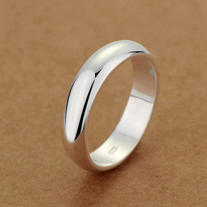 A sleek Rings Tibetan, crafted from polished 925 sterling silver, rests on a brown surface, its smooth, curved band reflecting light beautifully.