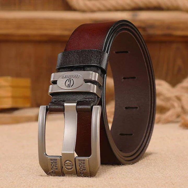 A Genuine Leather Belt with a high-quality silver buckle, embodying cowboy style with engraved text and an emblem, rests on a beige surface. The background is decorated with blurred wooden elements and textured fabric.