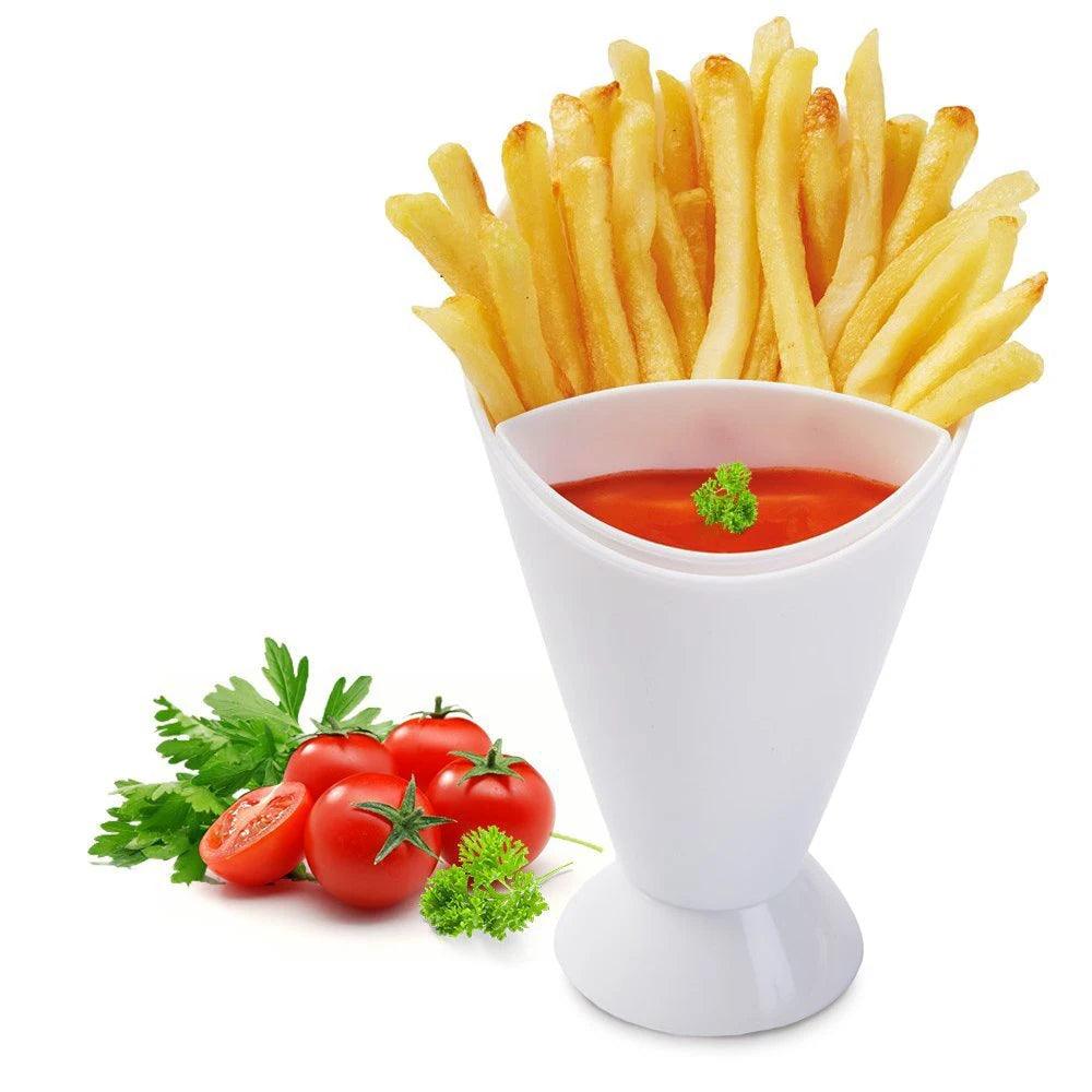 A cone-shaped white Snack Dipping Cup, known as the Sauce Storage Dish and crafted from plastic tableware, is filled with golden-brown fries. The base of the holder features a removable dipping tray filled with vibrant red ketchup. Fresh tomatoes and parsley are elegantly garnished beside the cup on a pristine white surface.