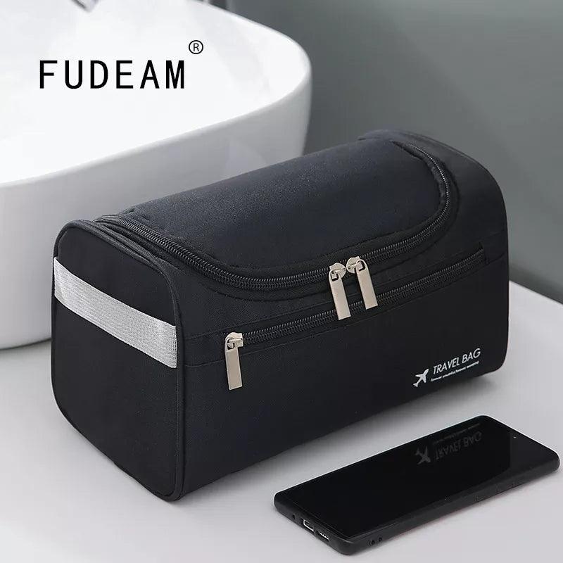 A black Men's Travel Toiletry Bag, with closed zippers, sits on a bathroom counter near a white sink. Featuring a small airplane symbol and the words "TRAVEL BAG," this waterproof Portable Toiletry Organizer is perfect for business trips. A smartphone rests in front of the Cosmetic Bag.