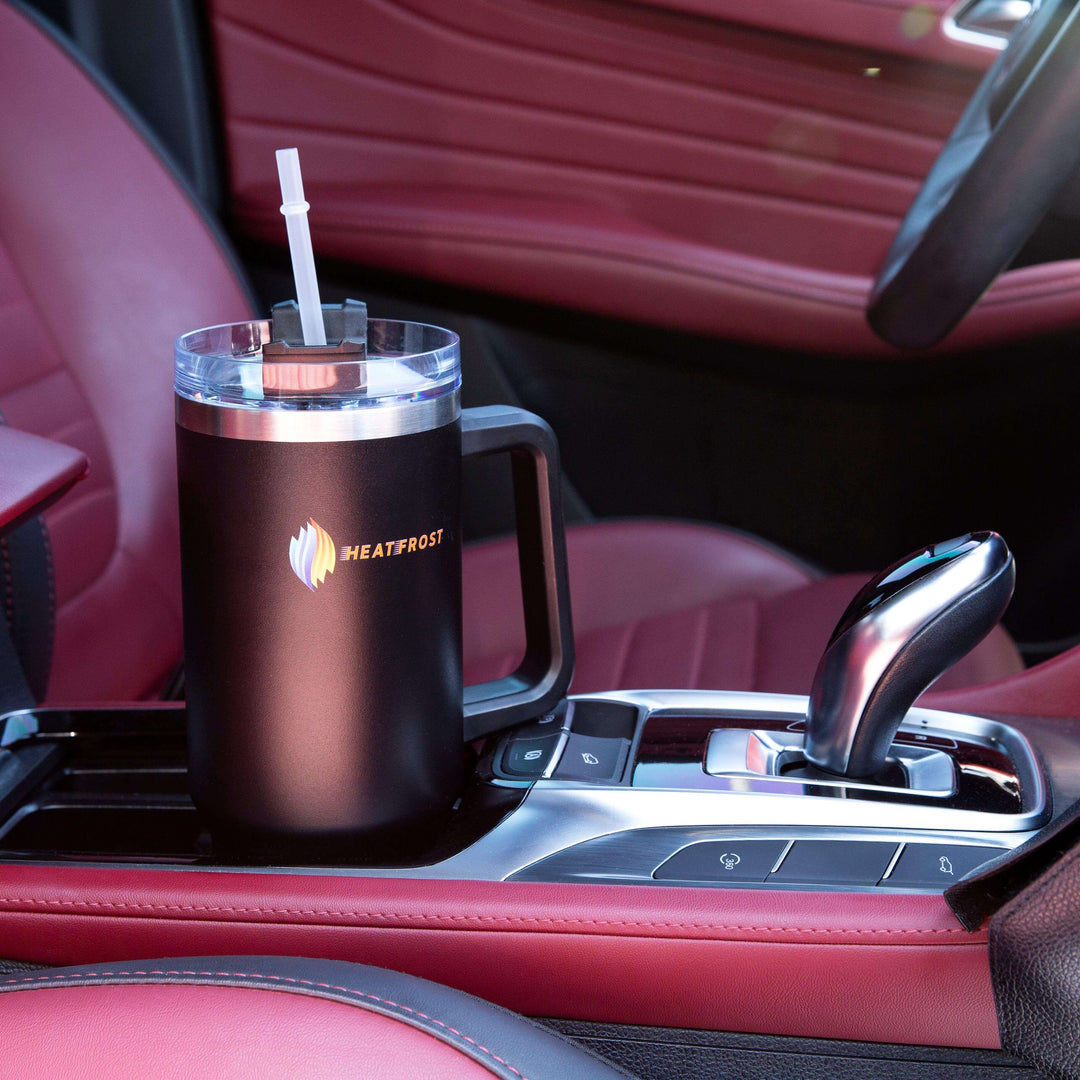 A sleek 40oz capacity Stainless Steel Tumbler, known as the Insulated Beverage Container Travel-Friendly Quencher, with a lid and straw fits perfectly in a car cup holder. Encased by a red interior featuring polished black accents, this tumbler displays HEATFROST's vibrant logo—a must-have for those who enjoy their drinks at the ideal temperature.