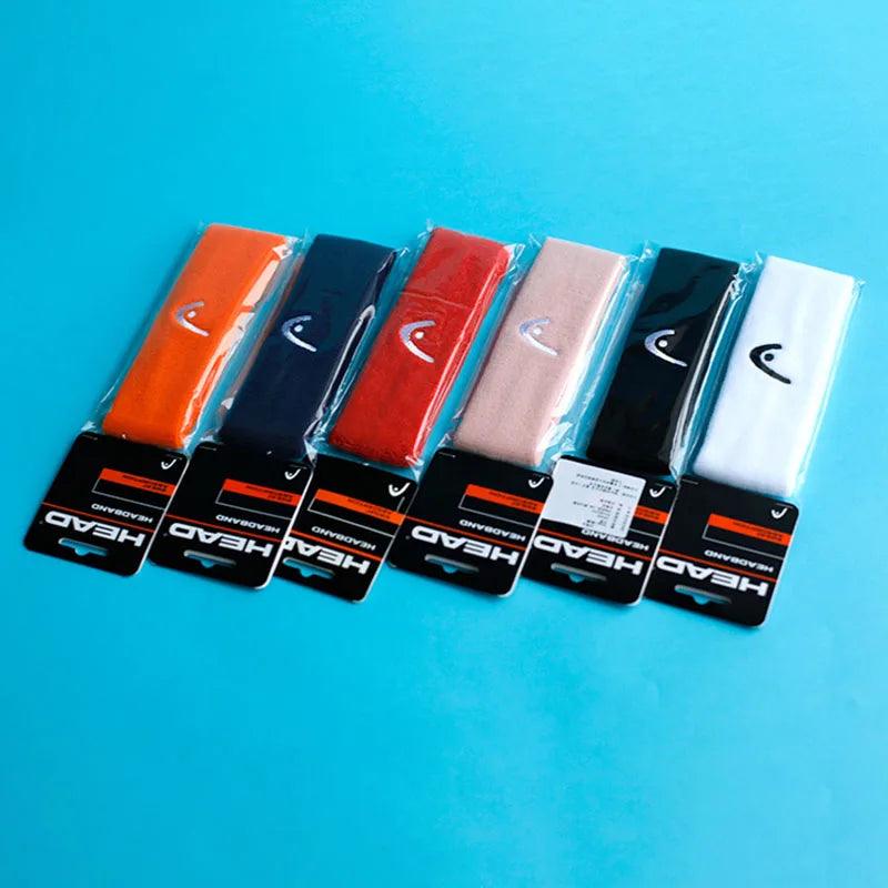 A row of six Exercise Headbands, available in orange, navy blue, red, beige, black, and white. These fitness sweat absorption belts are adorned with a small logo and a brand label displaying "HEAD." They are neatly arranged on a light blue surface.