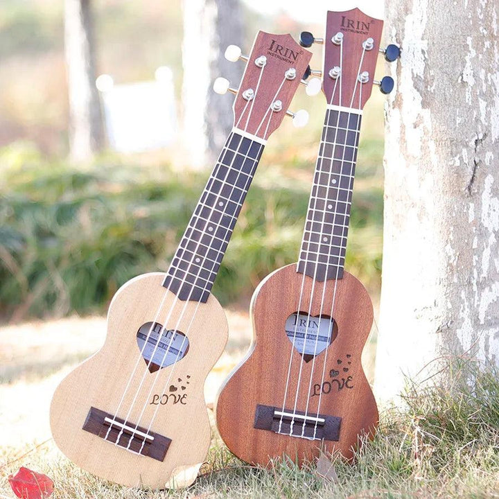 Two IRIN Ukuleles, featuring C-shaped necks and heart designs, rest against a tree. The lighter one is the 17 Inch Spruce Wood Ukulele Hawaiian Guitar, while the other is darker. Sunlight filters through, casting a warm glow on the grass and blurred scenery beyond.