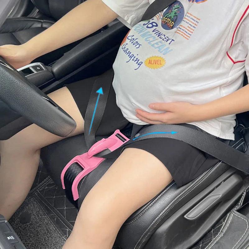 A person seated in a car is secured with a Pregnancy Car Seat Belt, which redirects the safety belt across the thighs instead of the abdomen. The individual gently touches their belly, hinting at pregnancy.