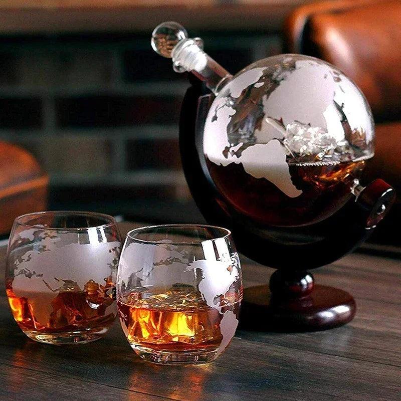 A world map-etched Whiskey Decanter Set, featuring a globe-shaped lead-free decanter filled with amber liquid and two matching whiskey glasses, rests elegantly on a polished wooden stand, inviting enthusiasts to enjoy their premium barware.