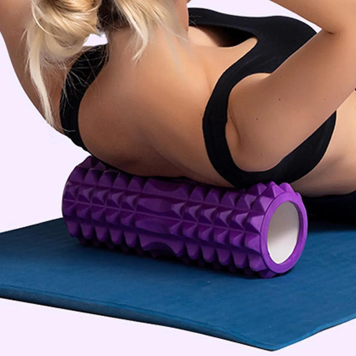 A person is utilizing a Yoga Column, which is a Fitness Equipment and Muscle Therapy Roller made of foam, on their back while lying on an exercise mat. They are wearing a black sports bra.