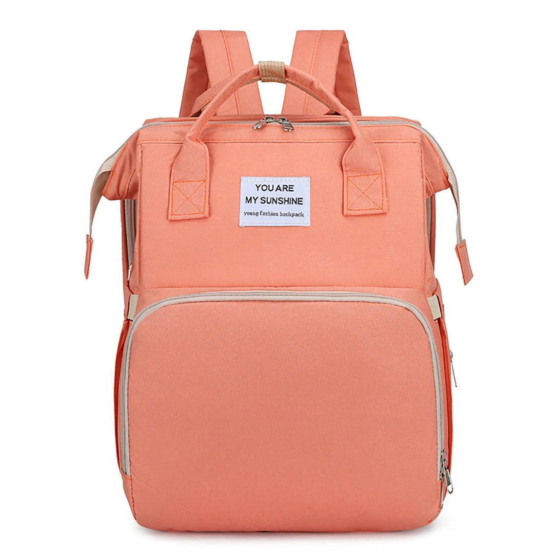 A chic peach-colored Portable Folding Bed Bag Multi-functional Mom Backpack with a front pocket and a "You are my sunshine" text label. This large capacity diaper bag is equipped with two shoulder straps, a top handle, and can conveniently transform into a portable folding bed for on-the-go ease.