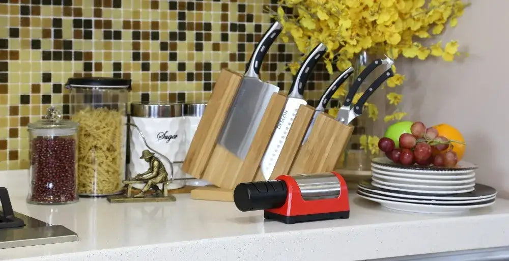 Electric knife sharpener on kitchen countertop next to knife block, pasta jar, and fresh fruit, showcasing a vibrant kitchen setup.