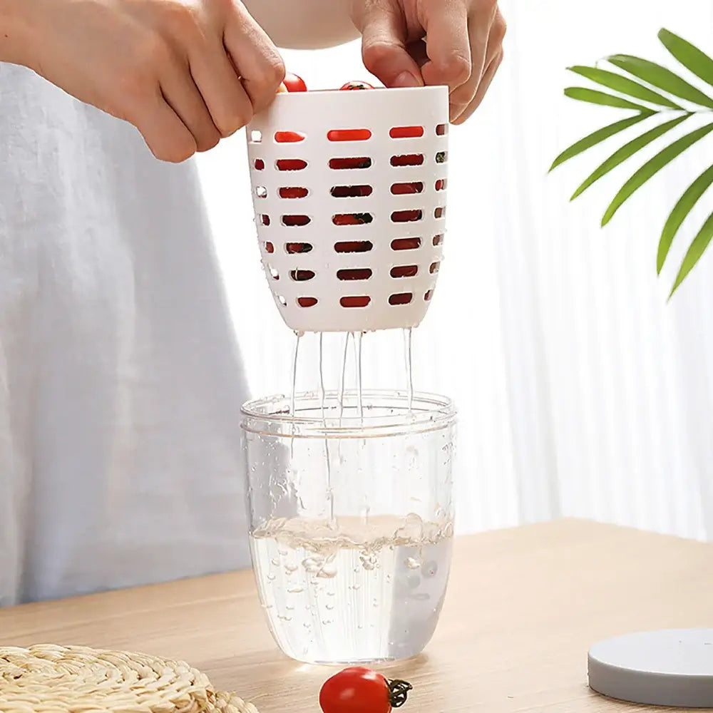 A person holds the "Fruit Cup with Fork Portable Picnic Bottle Large Capacity Storage Plastic Cup Sealed Leak Proof," which is eco-friendly and filled with cherry tomatoes, over a glass of water on a wooden table. The water drains effortlessly, allowing for spill-free storage. Nearby, a woven mat and green plant enhance the serene setting.