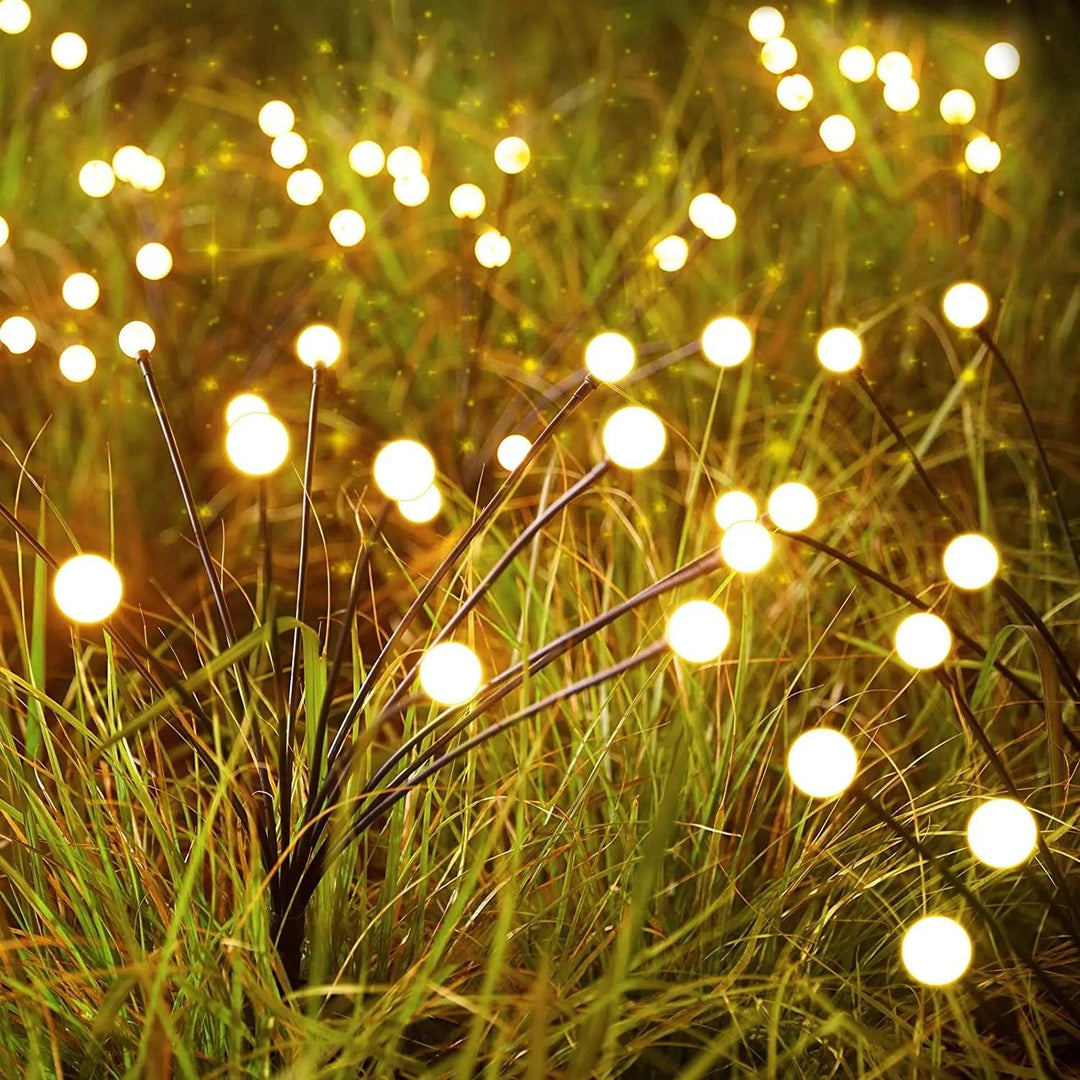 A field of soft-focused outdoor solar lights glows warmly among tall grass, creating a sparkling, magical atmosphere. The solar garden lights resemble fireflies scattered across the greenery, evoking a dreamy, enchanting night scene with reliable IP44 waterproof protection.