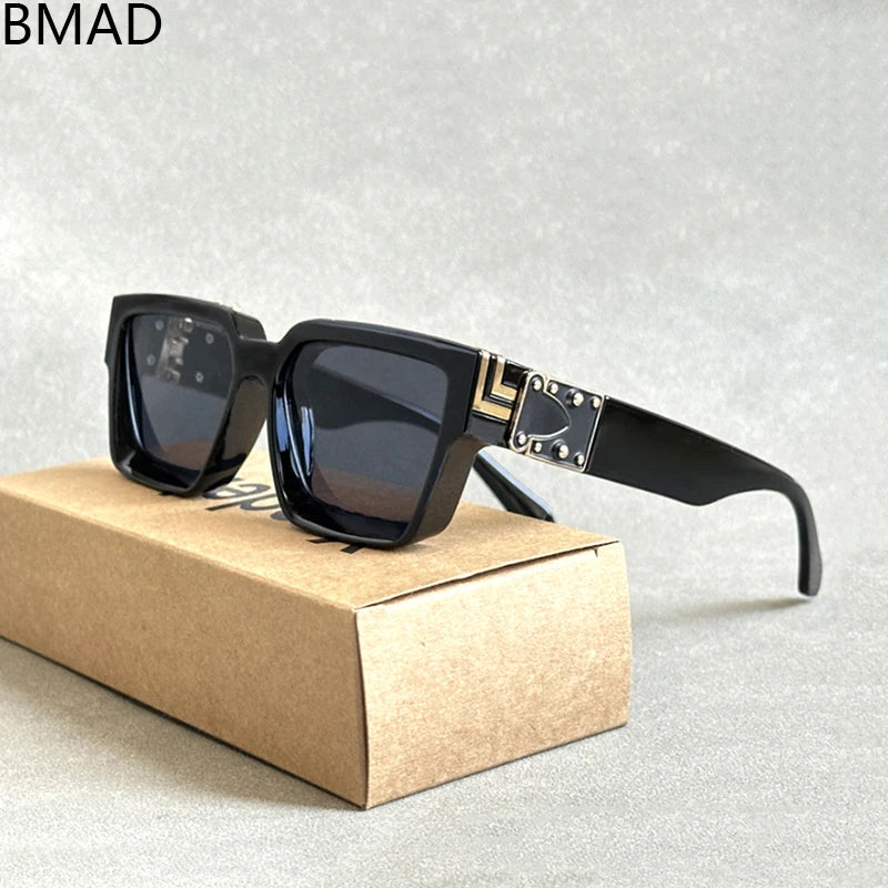 A pair of luxury designer square sunglasses from the collection "Sunglasses For Men Vintage Sunglasses Women," showcasing black frames with decorative gold accents on the arms, are elegantly displayed on a textured surface. These sunglasses provide UV400 protection and sit atop a simple brown cardboard case labeled BMAD.