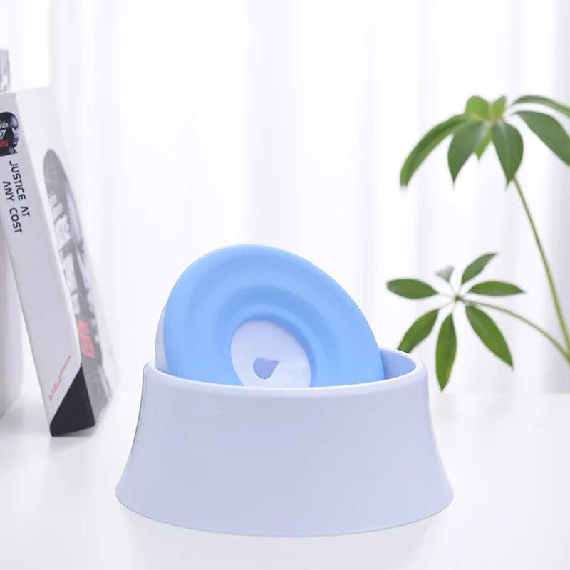 An Automatic Drinking Bowl, Splash-Proof Pet Feeder in blue and white stands on a table beside some books and a small plant. Its innovative design blends functionality with style, making it an ideal addition to any home. The background has sheer white curtains that bring an elegant touch to this practical accessory.