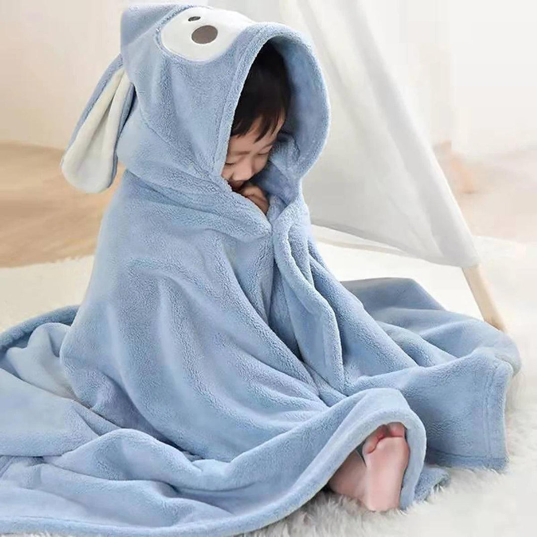 A newborn is snugly wrapped in a Children's Shower Skirt Newborn Baby Bathrobe, made from soft coral velvet, complete with a hood that features adorable bear ears and a charming bear face design. The child sits comfortably on a light-colored carpet, looking cozy and content, ideal for newborns.