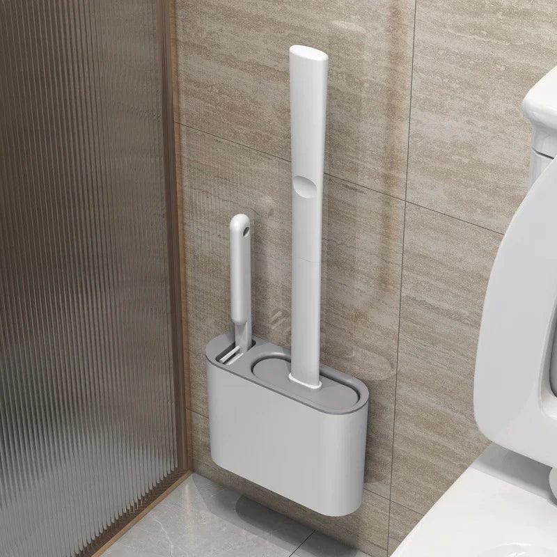 A Wall Hanging Toilet Brush with a long-handled silicone design is mounted on the bathroom wall, featuring a sleek, white toilet brush along with a smaller one in a compact holder. The beige tiles enhance the anti-adhesive coating, and part of the white toilet is visible in the corner.