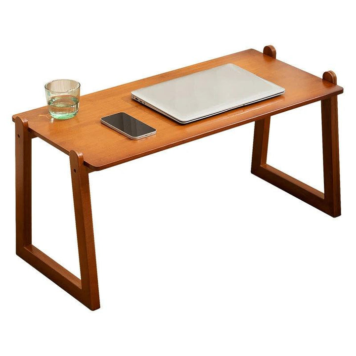 The Multi-functional Desk Student Computer Desk Portable Lap desk, crafted from sleek bamboo with foldable legs, supports a closed laptop, smartphone, and glass of water. This versatile desk exhibits a minimalist design and rests gracefully on a white background.