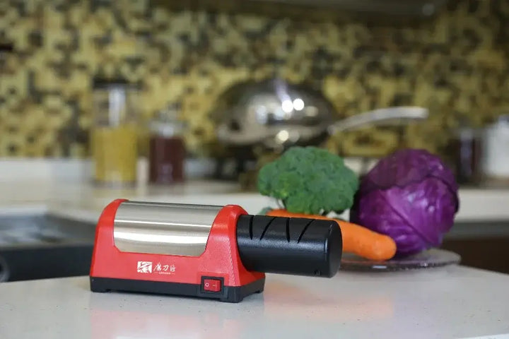 Electric knife sharpener on kitchen countertop with fresh vegetables in background.