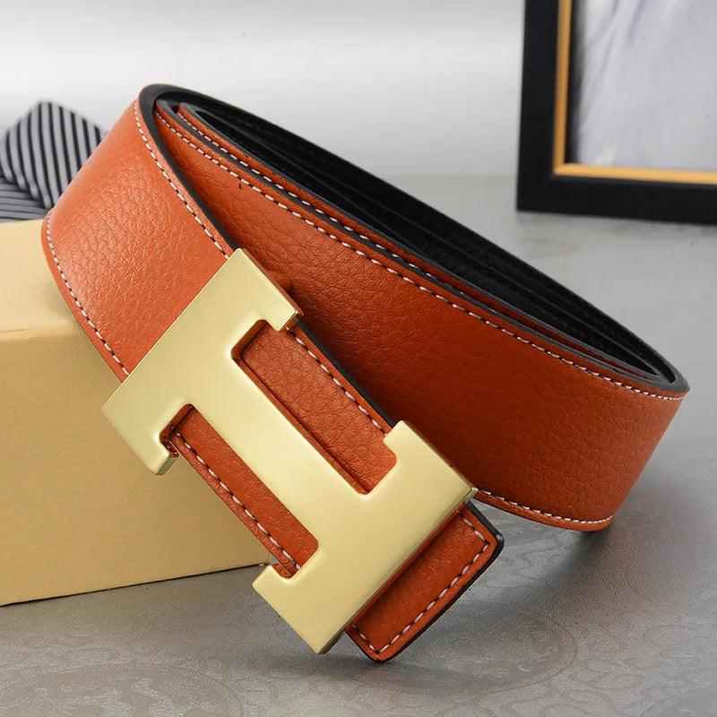 The men's leather belt, featuring a large gold "H" buckle, is elegantly coiled on a tan surface. Its rich brown hue exudes sophistication as its solid split leather texture and stitching are clearly visible. A framed picture and a striped bow tie sit behind it, complementing the scene.