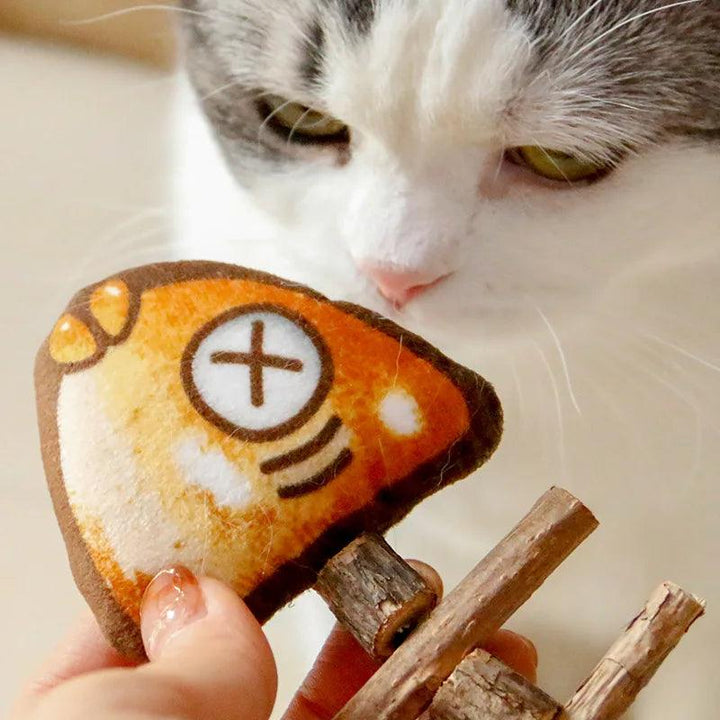 A curious cat sniffs at the Interactive Cat Teaser Toy, a Silvervine Grilled Fish Chew Kitten Play Accessory complete with an "X" eye design and vibrant orange finish. Held by a person's hand, this toy captures the cat's focused attention and playful curiosity.