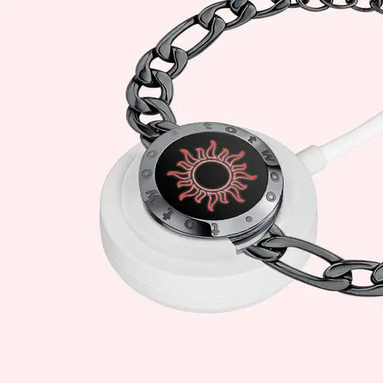 The Long Distance Bracelet Couple's Jewelry Interactive Love Gift is a stylish piece that connects beautifully with a white wireless charging pad. The metal chain is adorned with a circular black accent showcasing a red sun-like design, elegantly draping around the pad on a light background, making it perfect as an expressive gift for couples.