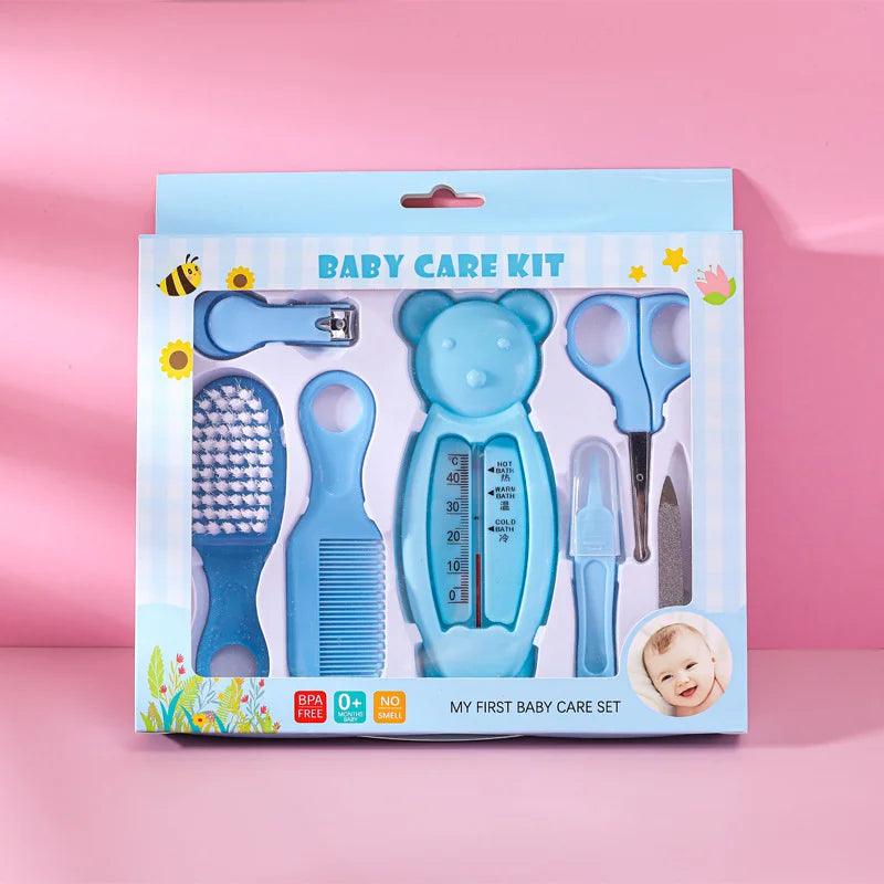 A blue Baby Care Kit, displayed on a pink background, contains essential baby care items such as a thermometer, nail clipper, scissors, hairbrush, comb, and nasal aspirator. Made from baby-safe plastic, the packaging is labeled "Baby Care Kit" and includes a small photo of a smiling baby in the corner.