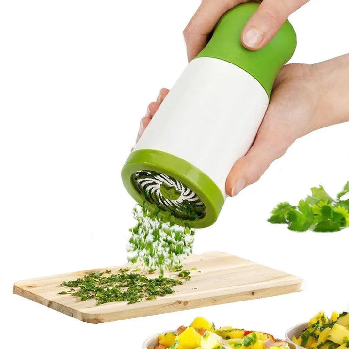 A person uses a Vegetable Grinder, Stainless Steel Pepper Grinder, Parsley Chopper to finely dice fresh herbs over a wooden cutting board. The stainless steel blades efficiently chop parsley. Nearby, there's a bunch of cilantro and a bowl of salad filled with vibrant vegetables at the bottom of the image.