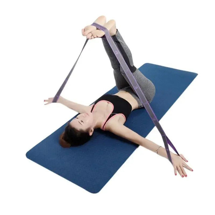 A woman is lying on an exercise mat, expertly performing a yoga stretch for posture correction. Clad in a black sports top and gray leggings, she skillfully holds the Yoga Pull Strap Belt, made from polyester-latex elastic band materials, using her feet while extending her arms wide. The blue mat contrasts with the plain white background, illustrating harmony.