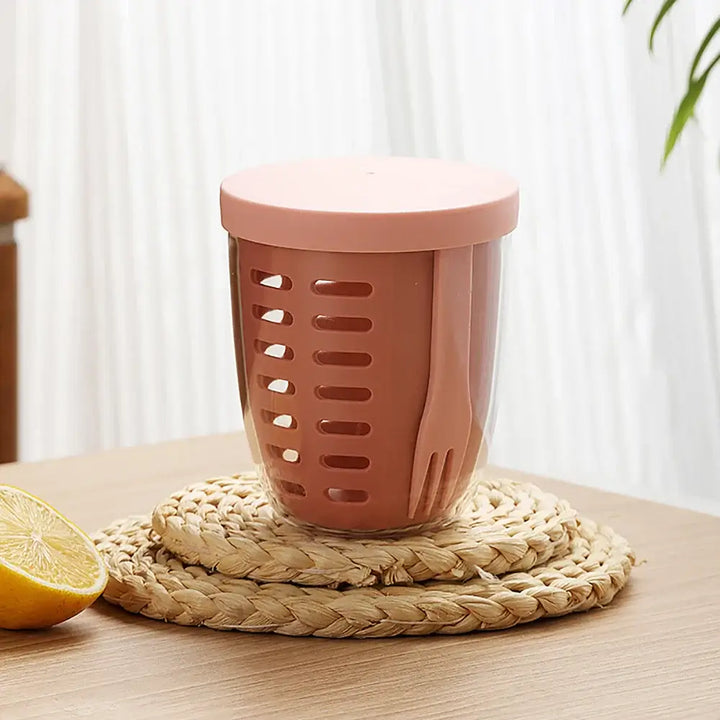 The "Fruit Cup with Fork Portable Picnic Bottle" in a charming pink hue rests on a straw coaster, featuring both a fork and spoon. This large-capacity, eco-friendly container doubles as a leak-proof salad box for your delicious creations.