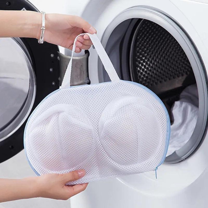 A person is placing the Protective Laundry Pouch, a delicate lingerie wash bag, into a front-loading washing machine. Crafted from durable mesh and polyester with two compartments and featuring a convenient handle, this laundry bag makes laundry day effortless as the washing machine door stands open, ready for action.