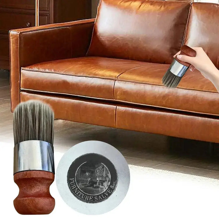 A hand holding a brush gently applies Owl Furniture Salve Leather Cleaner to a brown leather couch. In the foreground, a close-up of the salve container and brush showcases how the wooden handle complements the rich leather upholstery.