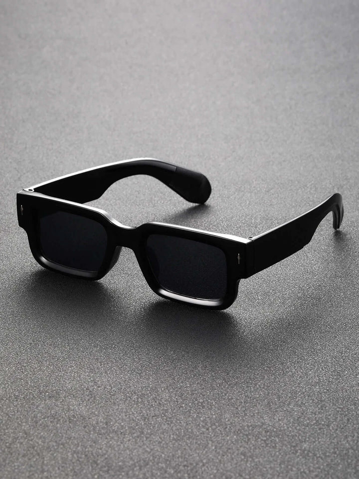 The Square Plastic Frame Sunglasses in black, featuring thick frames and UV400 protective plastic lenses, rest on a textured gray surface. The dark lenses stand out sharply against the slightly reflective background beneath.