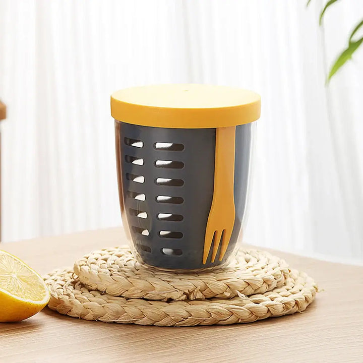 A glass container, complete with a yellow lid and fork, elegantly sits on a straw coaster, designed as an eco-friendly, leak-proof salad box similar to the "Fruit Cup with Fork Portable Picnic Bottle Large Capacity Storage Plastic Cup Sealed Leak Proof.