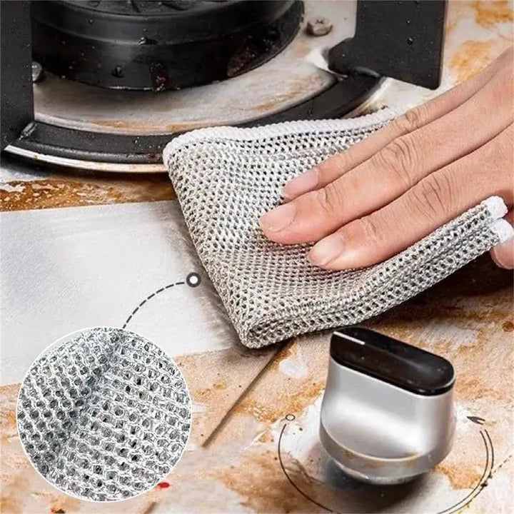 Hand using magic cleaning cloth to scrub stovetop; close-up of thickened double-sided metal steel wire texture.