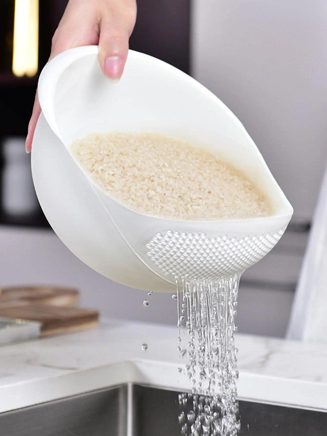 A person pours water from a Kitchen Rice Washing Strainer with a white grid-like design, ideal for efficient draining. Water flows into the sink below, demonstrating its function as an essential kitchen organizer for fruits and vegetables.