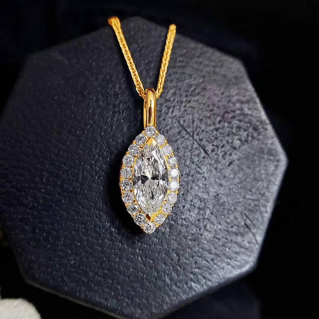 A Marquise Moissanite Necklace Moissanite Pendant Gemstone Necklace features a pendant highlighted by smaller clear stones, elegantly presented on a dark octagonal surface. The gold chain adds to the sophistication of this exquisite piece.