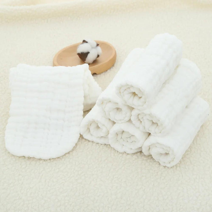 A stack of neatly rolled, soft white towels is placed on a cream-textured surface. Beside them lies a piece of folded fabric, a small wooden dish with a cotton boll atop it, and Cotton Cloth Diaper Inserts Reusable Nappy Liners Absorbent Diaper Inserts ready for use.