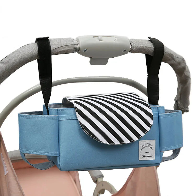 A "Stroller bag organizer" made from premium nylon fabric in blue hangs on a stroller handle. It features a black and white striped flap, multiple pockets for plenty of storage space, and durable black straps.