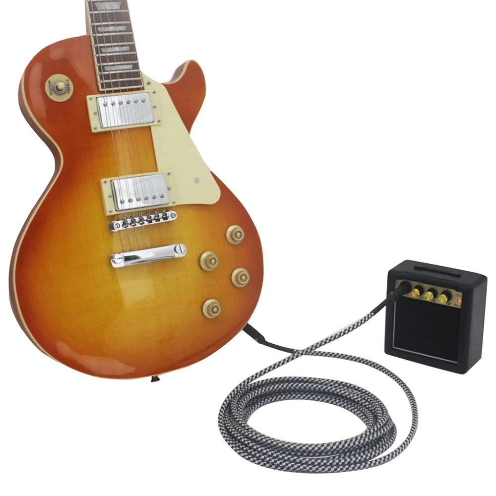 A sunburst electric guitar connects to a Mini Guitar Amplifier, Portable Guitar Speaker, Acoustic Electric Guitar Amp using a long, coiled cable. The guitar, boasting the iconic Les Paul shape, includes two humbucker pickups, four control knobs, and a selector switch. The compact amp offers precise sound control with its four dials on top.