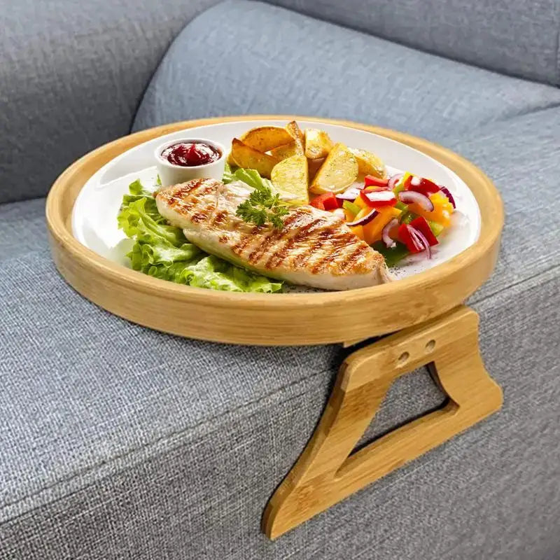 A Natural Bamboo Sofa Tray, designed as a Sofa Armrest Clip-On Tray, elegantly rests on the gray sofa. This TV Snack Tray serves a meal featuring grilled chicken, potato wedges, sliced peppers, and a small cup of ketchup, all garnished with parsley.