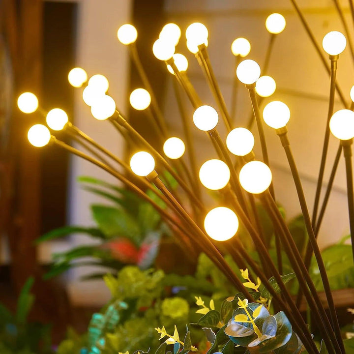 A collection of the "Warm white solar lights" featuring glowing orbs on long stems is placed among lush green foliage. These orbs provide a warm, inviting glow through LED bulbs, enhancing the serene and magical atmosphere while waterproof protection ensures that the "Outdoor solar lights" are durable in any weather.