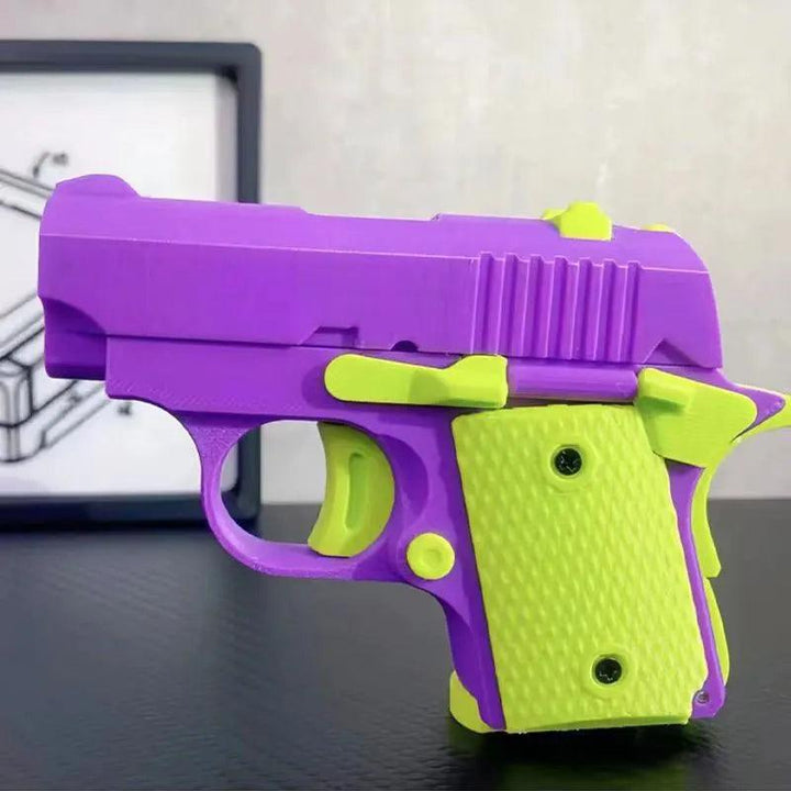 The "Mini 1911 toy gun," featuring a primarily purple body accented with lime green on the handle and trigger, is made from non-toxic materials, showcasing realistic grooves and textures. It rests on a dark surface with a blurred framed sketch visible in the background.