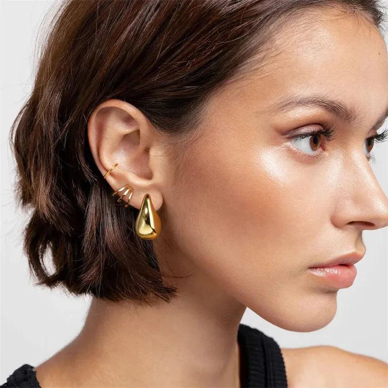 A woman with short brown hair wears the Vintage Gold Drop Earrings, showcasing a striking teardrop shape complemented by a smaller gold spiral. Her look is natural and elegant as she is pictured from the side against a plain background.