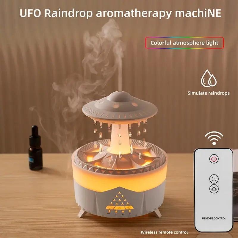 A humidifier, the Humidifier Water Drop Air with a design reminiscent of an alien spaceship, rests on a table, emitting mist and colorful night light effects. It showcases simulated raindrop elements and comes with a wireless remote control. An Essential Oils Aroma bottle is nearby, prepared to enhance your aromatherapy experience.