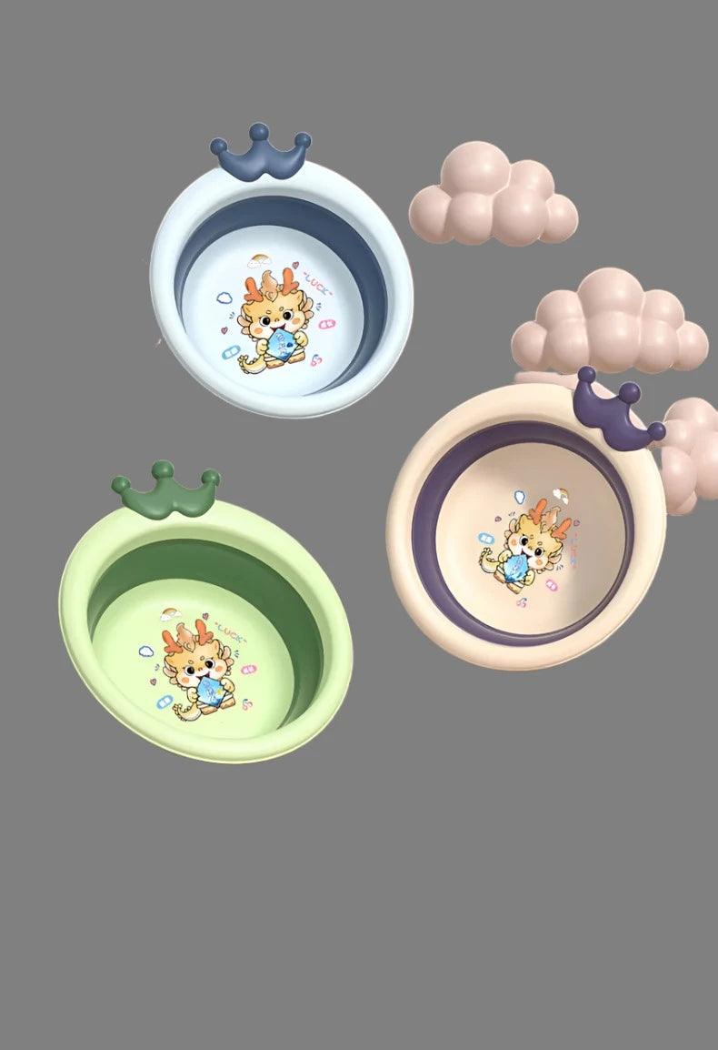 Three "Foldable baby basins" with round, crown-shaped handles are arranged on a grey background. Each "Newborn wash basin" displays cartoon patterns of a giraffe holding a ball. Soft, plush clouds enhance the whimsical effect surrounding these vibrant items from the "Children's wash set.