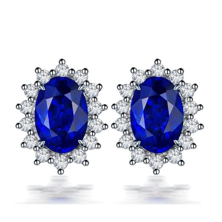 A pair of elegant earrings featuring large oval blue gemstones, encircled by a halo of sparkling Cubic Zirconia stones, set in a lustrous Tibetan silver-toned metal.