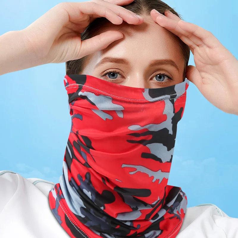 Wearing a red, black, and gray camouflage-patterned "Motorcycle neck cover," a person covers their lower face. They grasp the top edge with one hand against a blue sky backdrop.